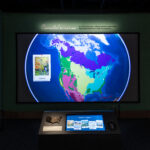 A colorful map of the United States of America is displayed on a large screen, labeled "Connected by Nature." Below the map is a touch screen saying, "Select a Map."